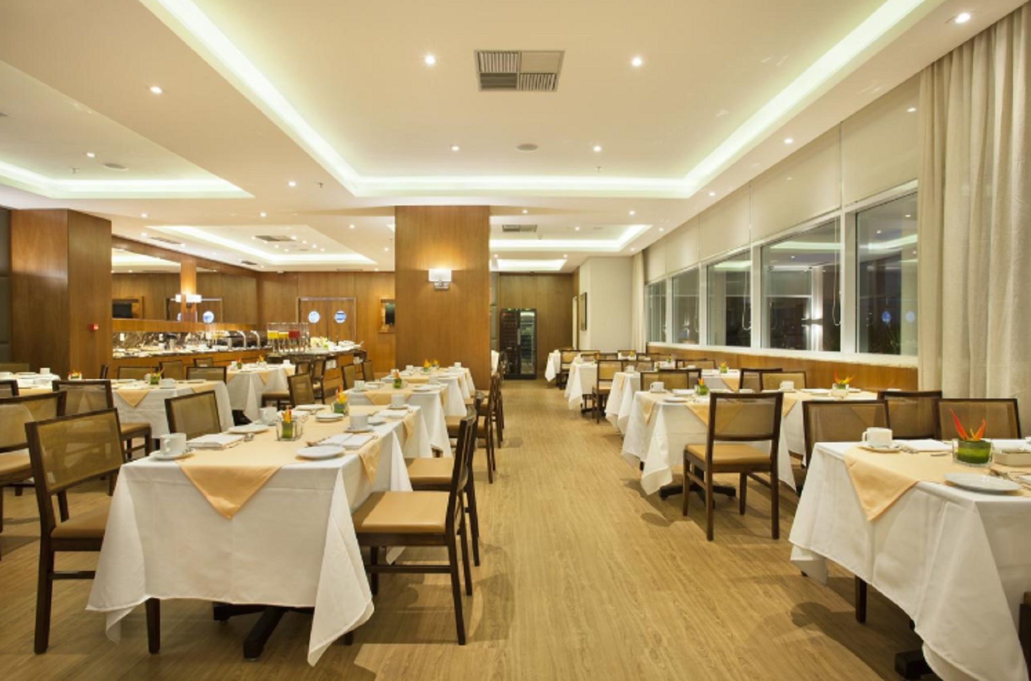 Ein großer Speisesaal mit mehreren Tischen und Stühlen, die in Reihen angeordnet sind, und einem Buffet im Hintergrund.