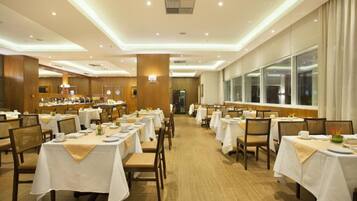 Ein großer Speisesaal mit mehreren Tischen und Stühlen, die in Reihen angeordnet sind, und einem Buffet im Hintergrund.