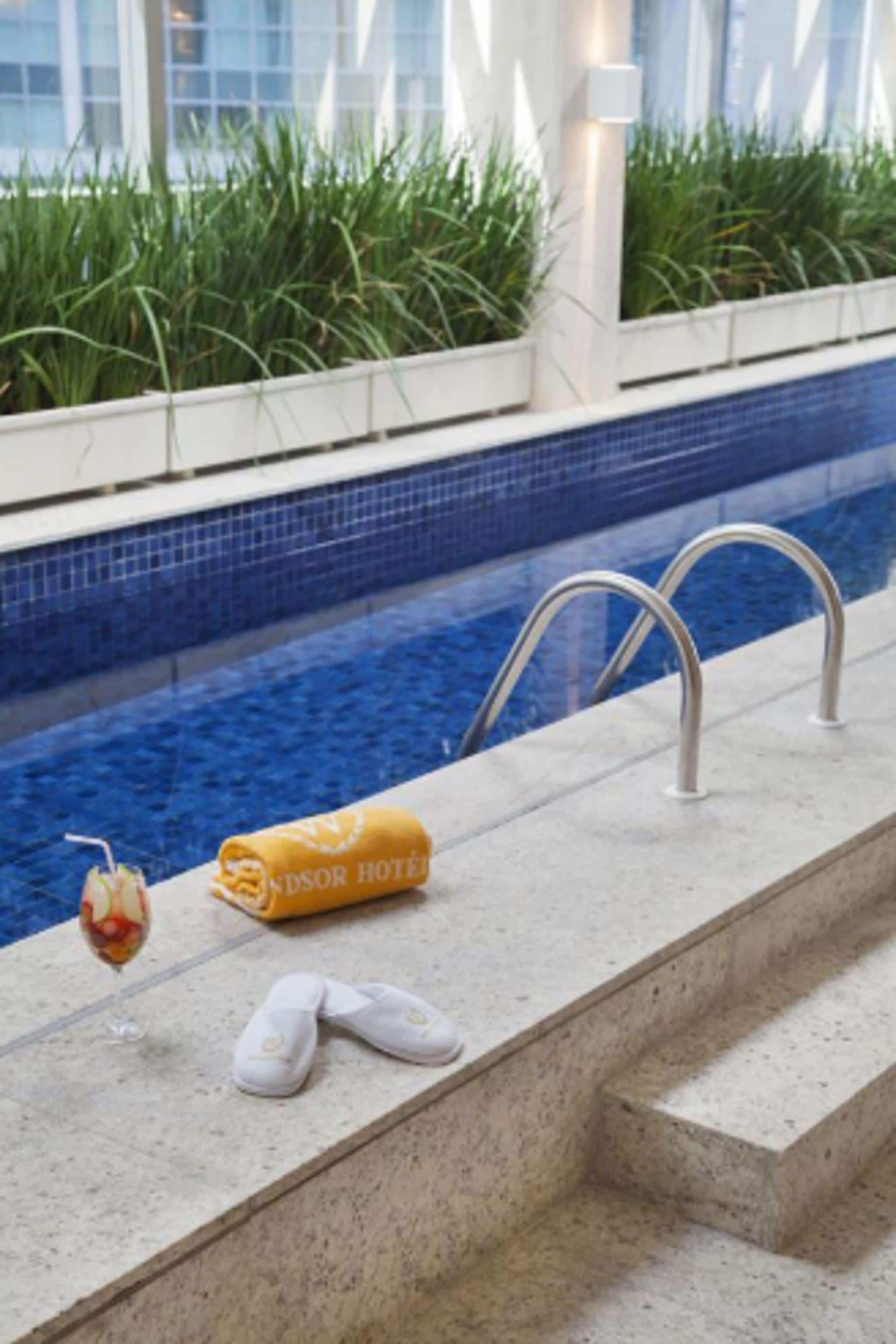 Ein Poolbereich mit klarem, blauem Wasser, einem Handtuch, Hausschuhen und einem Getränk.