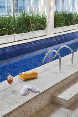 Un espace aménagé au bord de la piscine, avec une piscine à l’eau cristalline, une serviette, des chaussons et une boisson.
