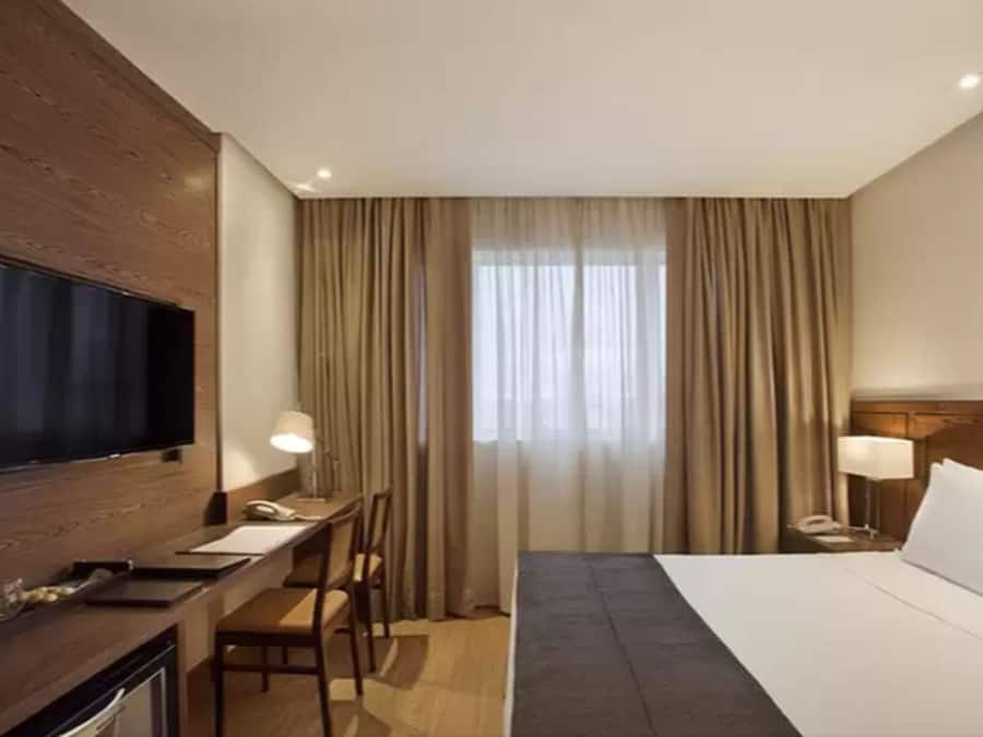 A hotel room with a bed, a desk, a television, and curtains.