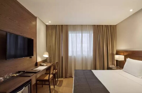 Une chambre d’hôtel avec un lit, un bureau, une télévision et des rideaux.