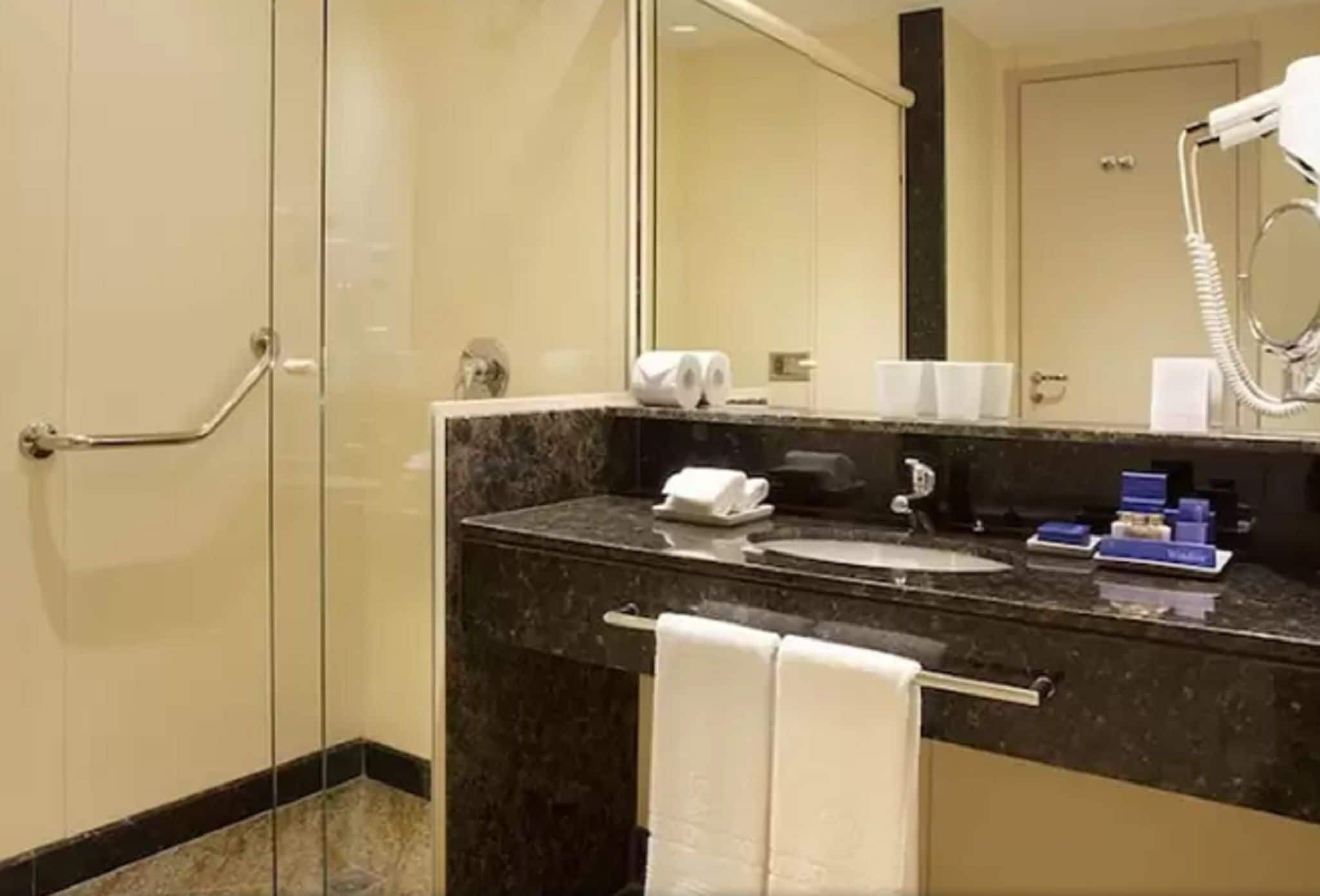 Un baño moderno con encimera de mármol, un lavabo, un espejo, un perchero para toallas y un secador de pelo.
