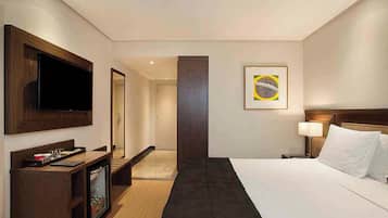 Een hotelkamer met een bed, een televisie, een bureau, een spiegel, een deur en een muur met een ingelijste afbeelding.