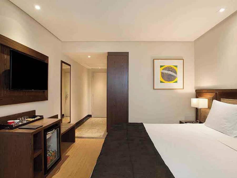 Een hotelkamer met een bed, een televisie, een bureau, een spiegel, een deur en een muur met een ingelijste afbeelding.