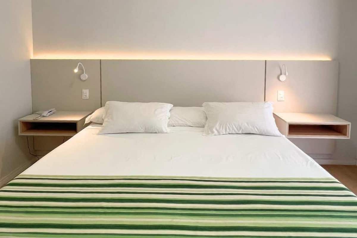 A hotel room with a large bed, two bedside tables, and wall-mounted reading lights.