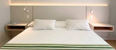 Una habitación de hotel con una cama grande, dos mesitas de noche y lámparas de lectura fijadas en la pared.