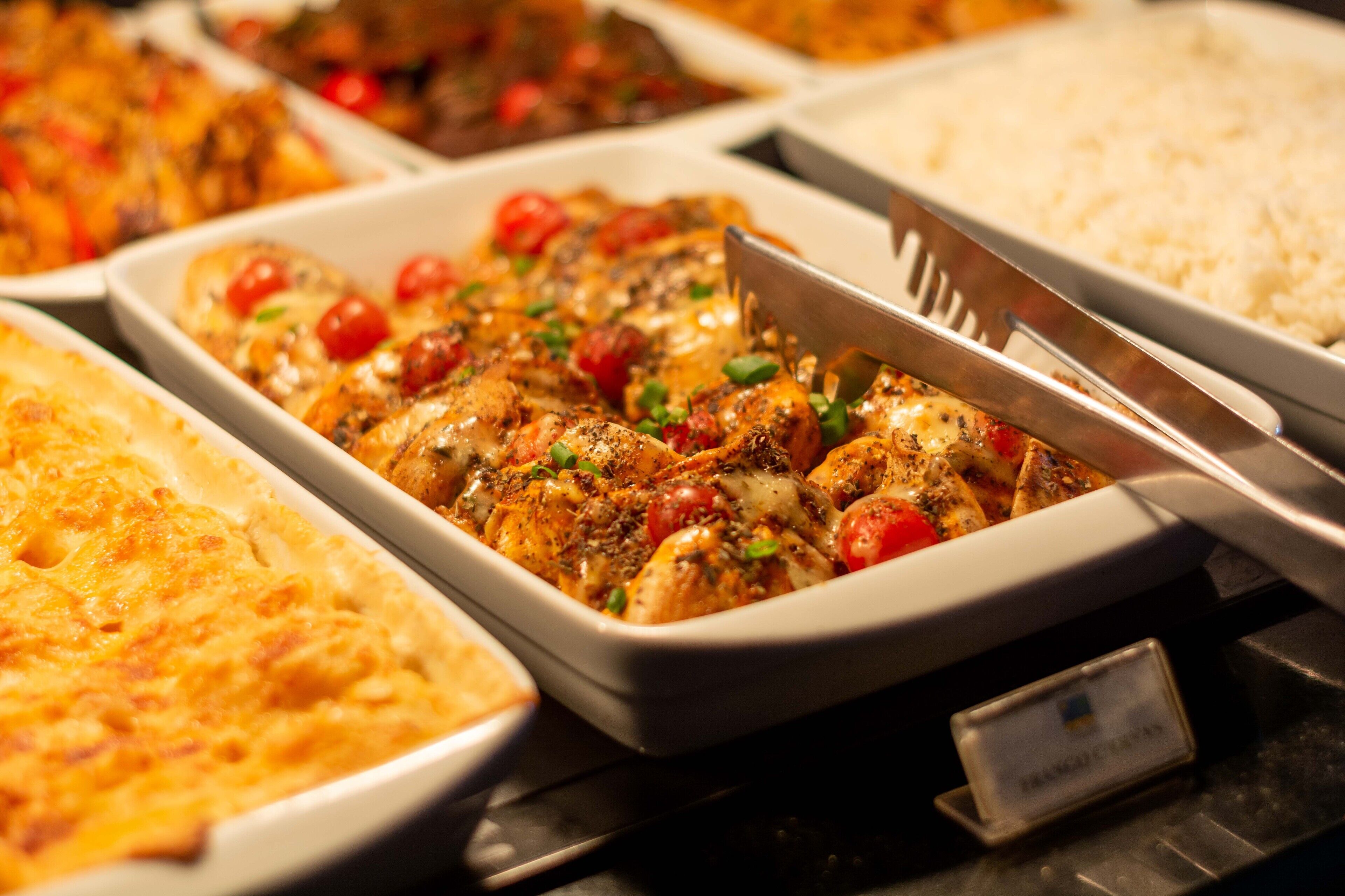 Un bufé con diversos platos, incluyendo un pastel de carne, arroz y un plato con pollo y tomates.