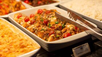 Un bufé con diversos platos, incluyendo un pastel de carne, arroz y un plato con pollo y tomates.