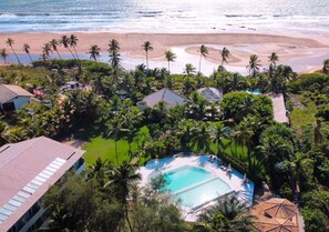 An aerial view of a resort with a central swimming pool, surrounded by palm trees and a beach. - Hotel Resort Costa Dos Coqueiros (Mata de São João)