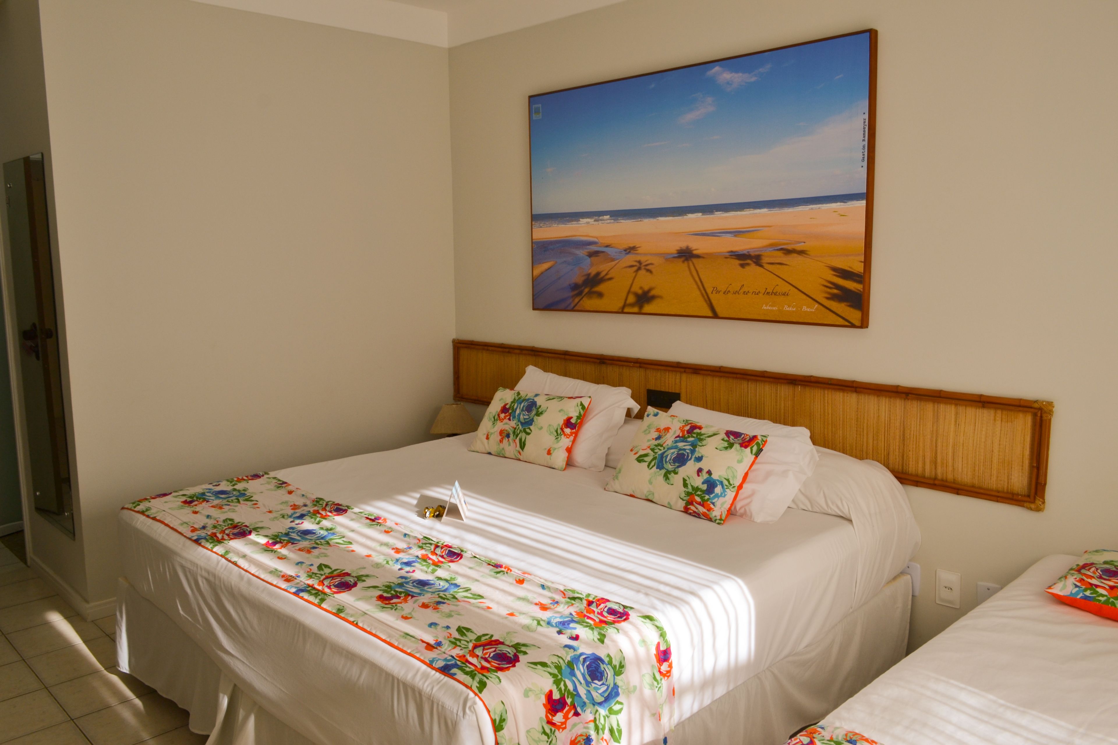 A hotel room with a large bed, a headboard, and a painting of a beach scene on the wall.