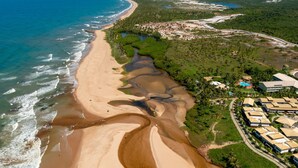 Vista aérea de una zona costera con una playa de arena, un pequeño poblado con edificios y una carretera que lleva a la playa.