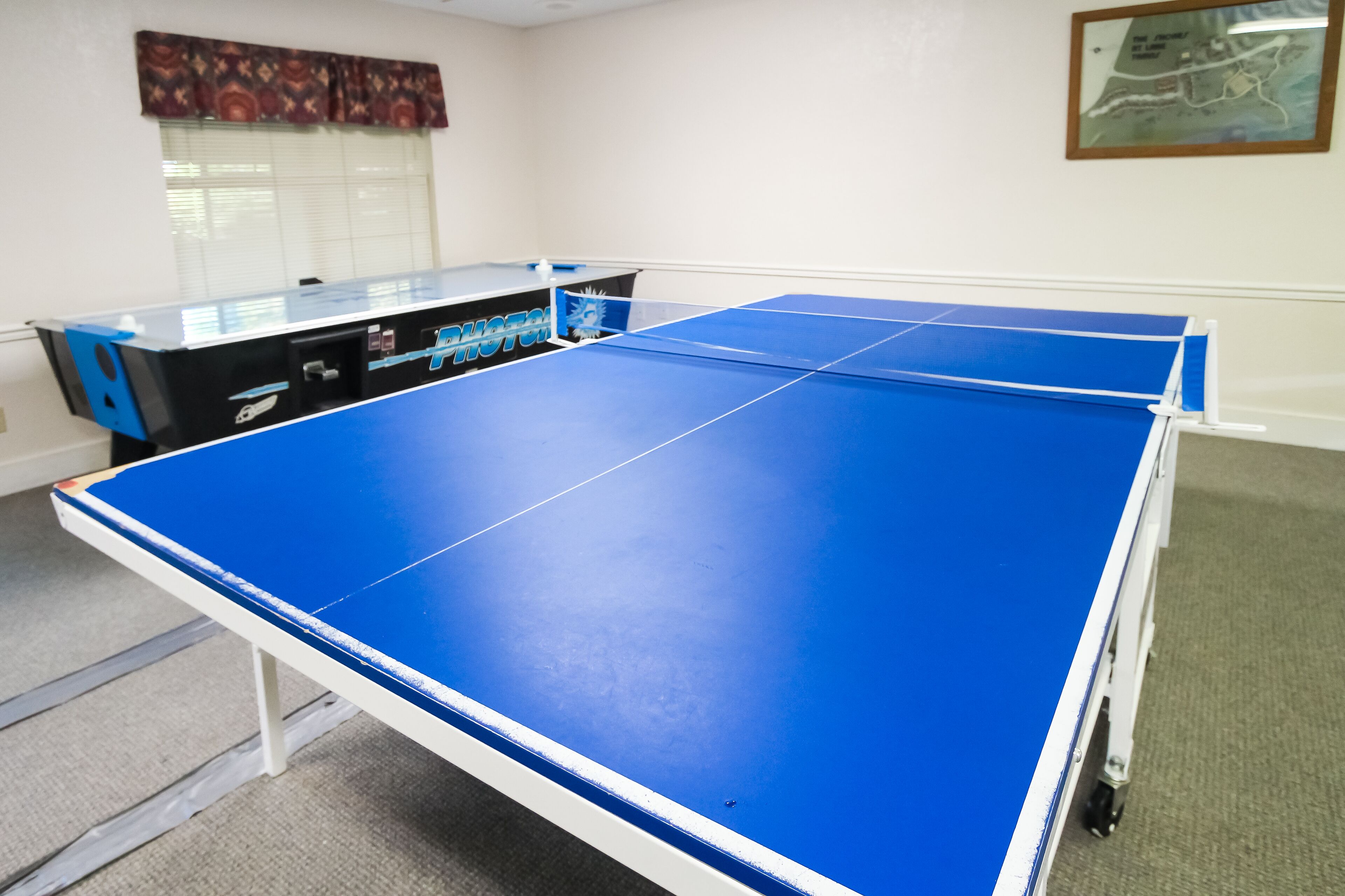 Una taula de ping-pong a una habitació amb una finestra, un mapa a la paret i una taula de tenis de taula.