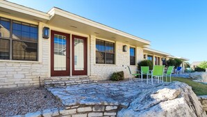 A building with a stone facade, a red door, and a patio area with green chairs. - The Shores at Lake Travis (Leander)