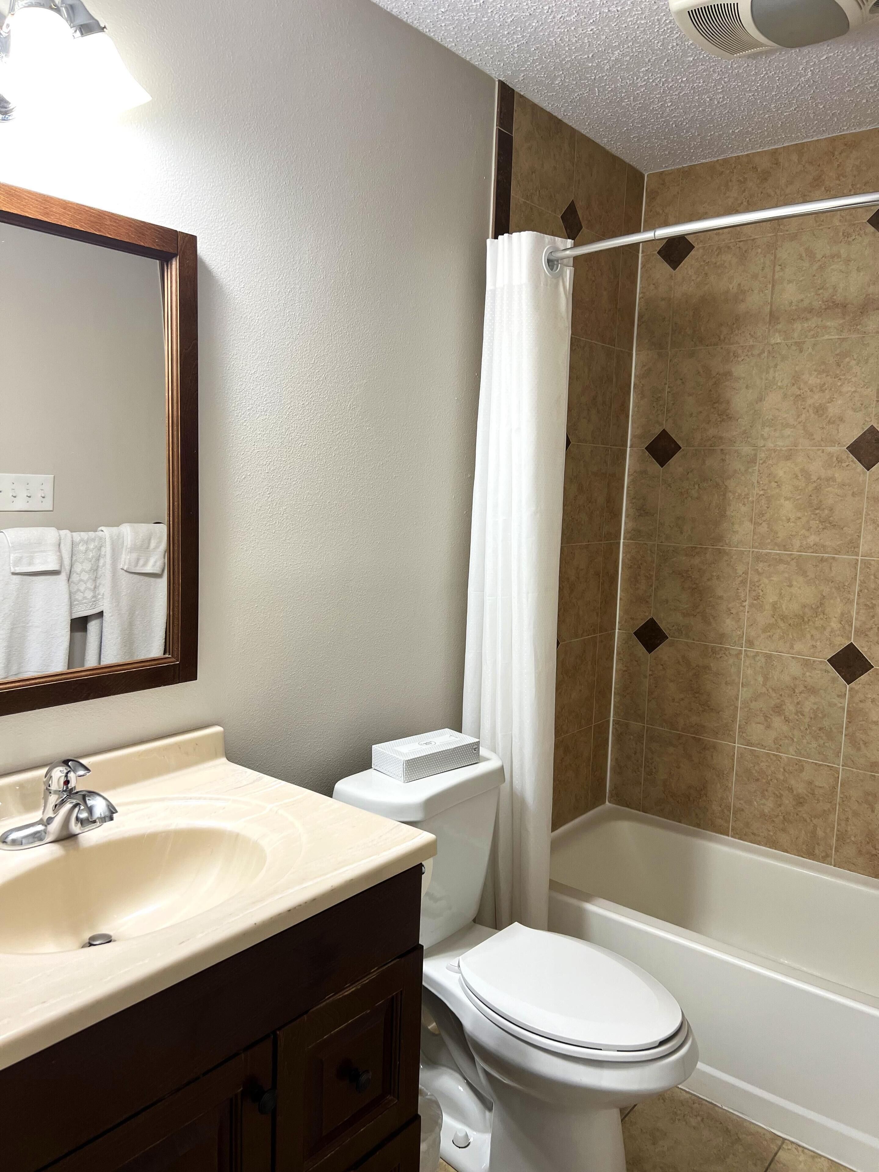 A bathroom with a sink, mirror, toilet, and bathtub.