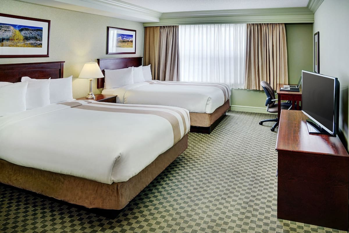 A hotel room with two beds, a desk with a computer, a TV, and a window with curtains.
