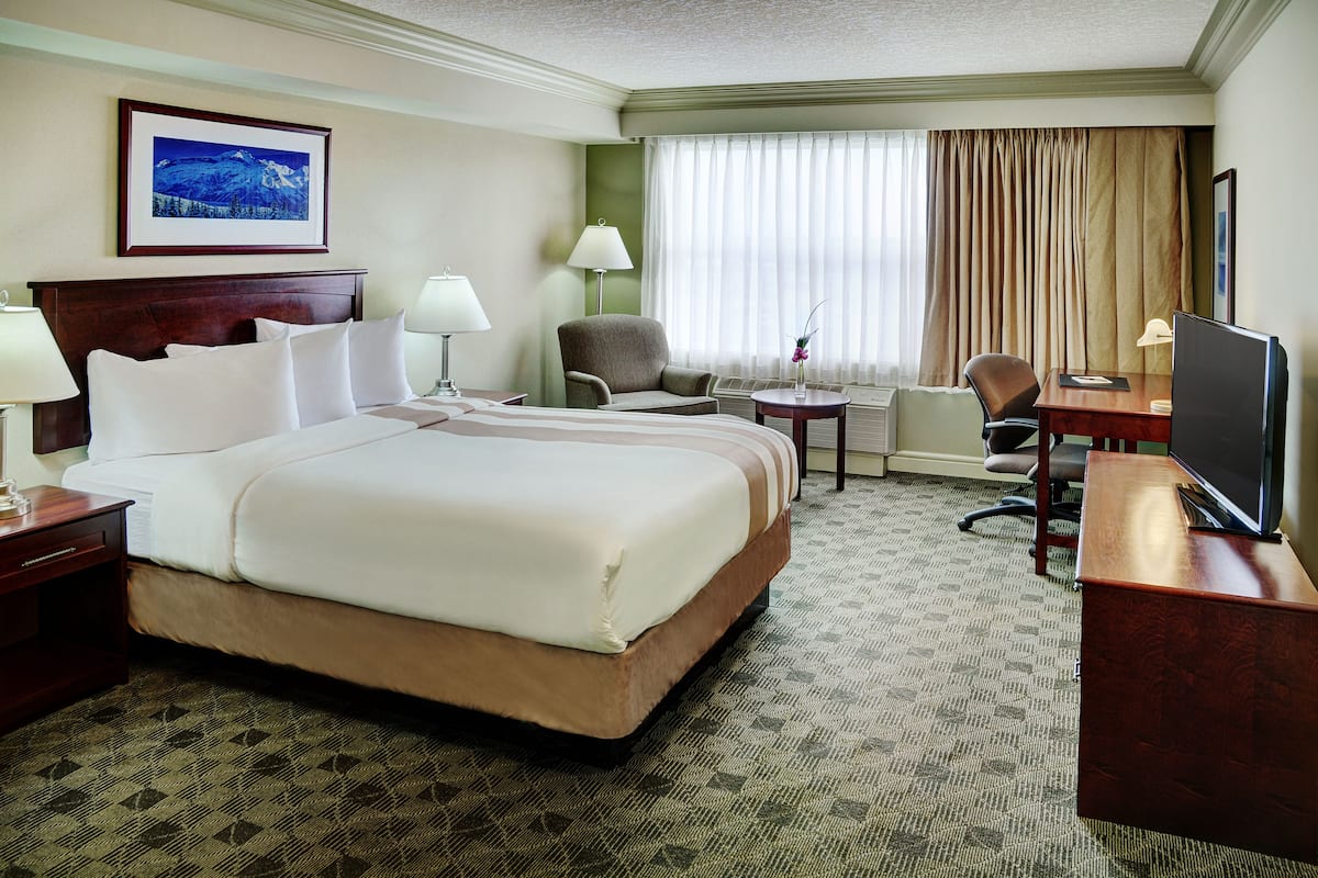 A hotel room with a large bed, two chairs, a desk with a TV, a lamp, and a painting on the wall.