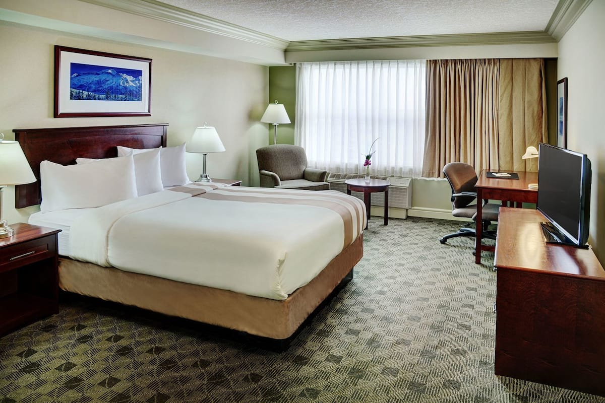 A hotel room with a large bed, two bedside tables, a desk with a chair, a television, and a window with curtains.
