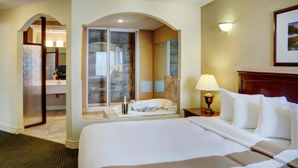 A hotel room with a large bed, a glass-enclosed shower, a bathtub, and a bedside table with a lamp. - Chateau Nova Kingsway (Edmonton)