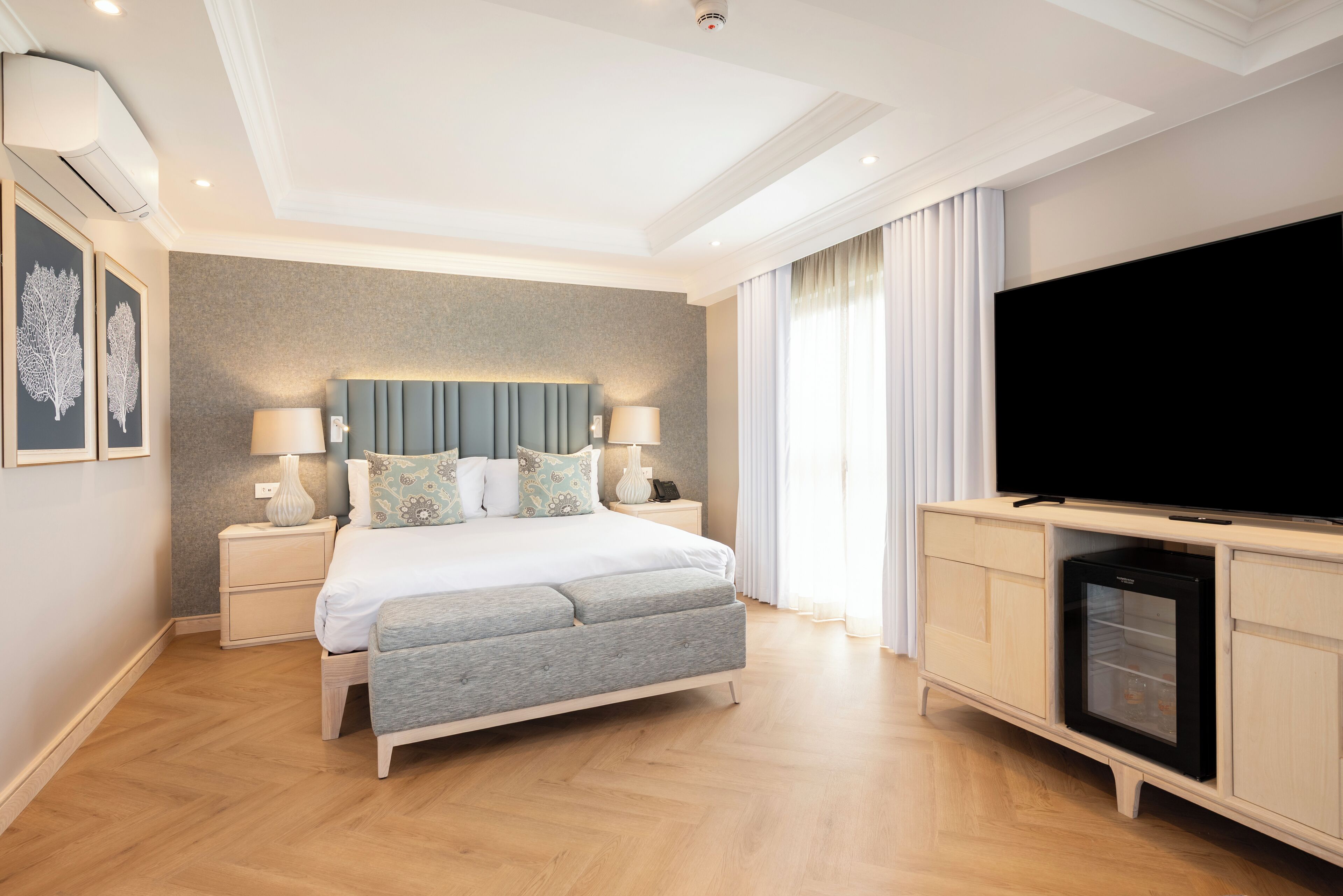 A modern bedroom with a bed, bedside tables, a TV, and a minibar.