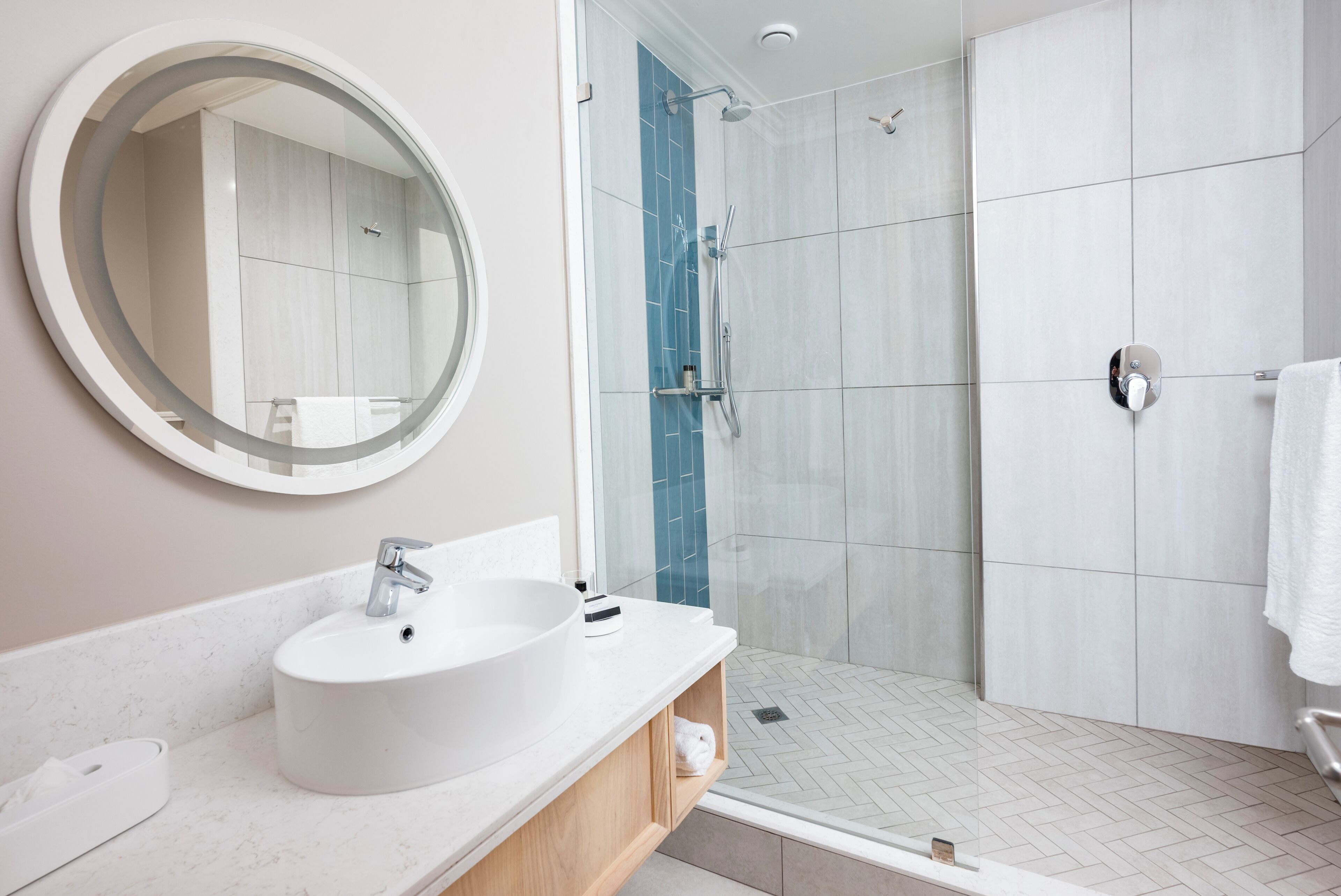 A modern bathroom with a large round mirror, a white sink, and a shower area.