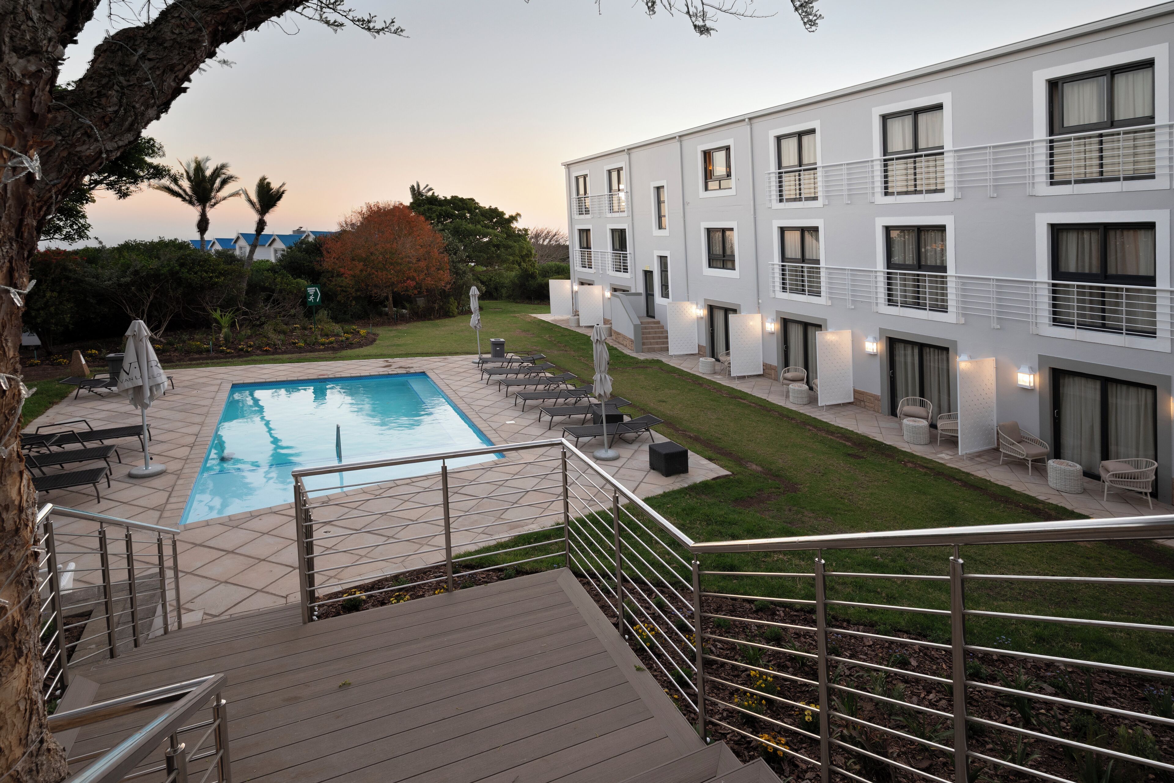 A modern hotel with a swimming pool, outdoor seating, and a well-maintained lawn.