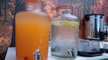 Two glass jars with taps, one filled with orange liquid and the other with clear liquid, and a coffee maker on a white surface.