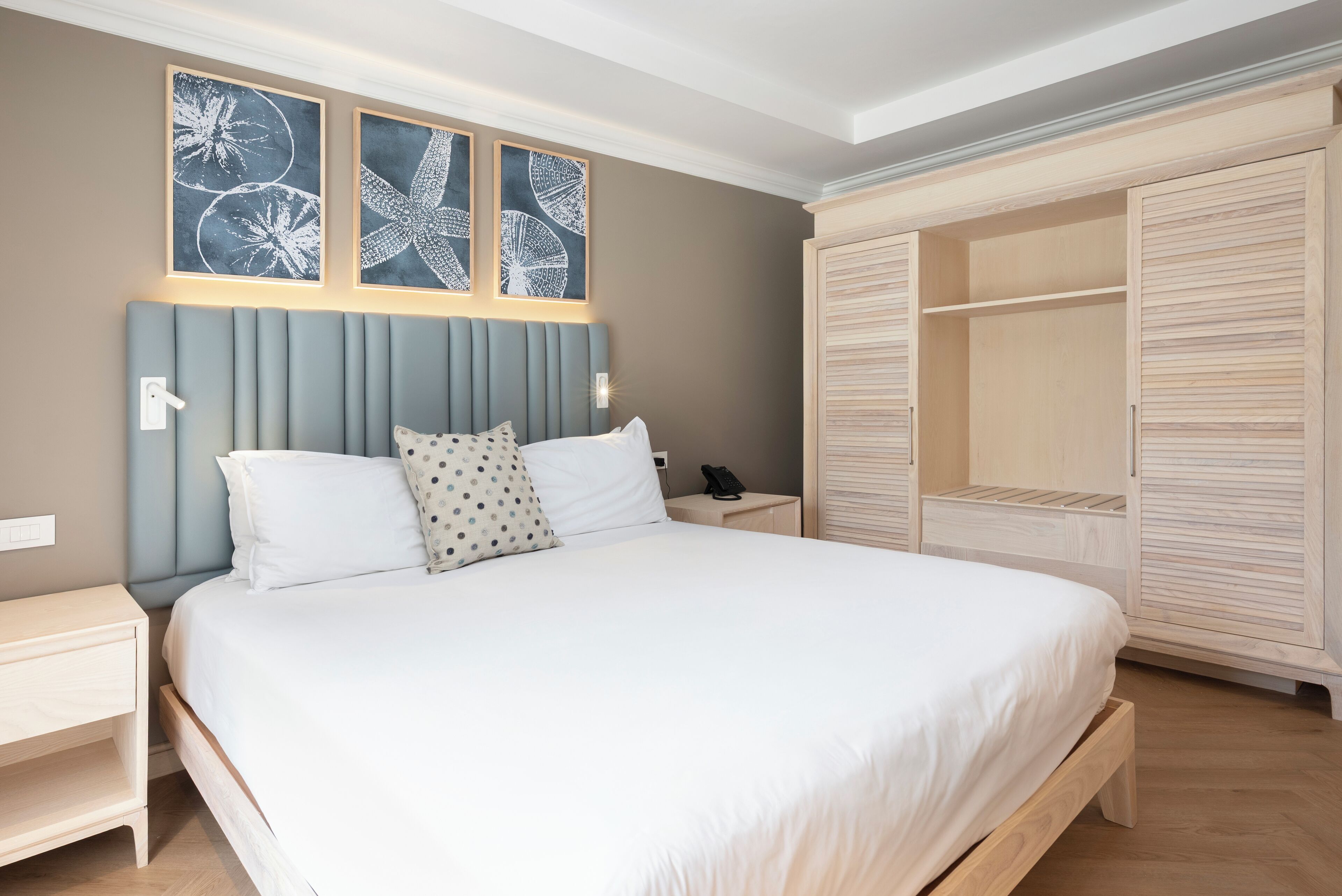 Een slaapkamer met een bed, nachtkastjes, een kledingkast en kunst aan de muur.