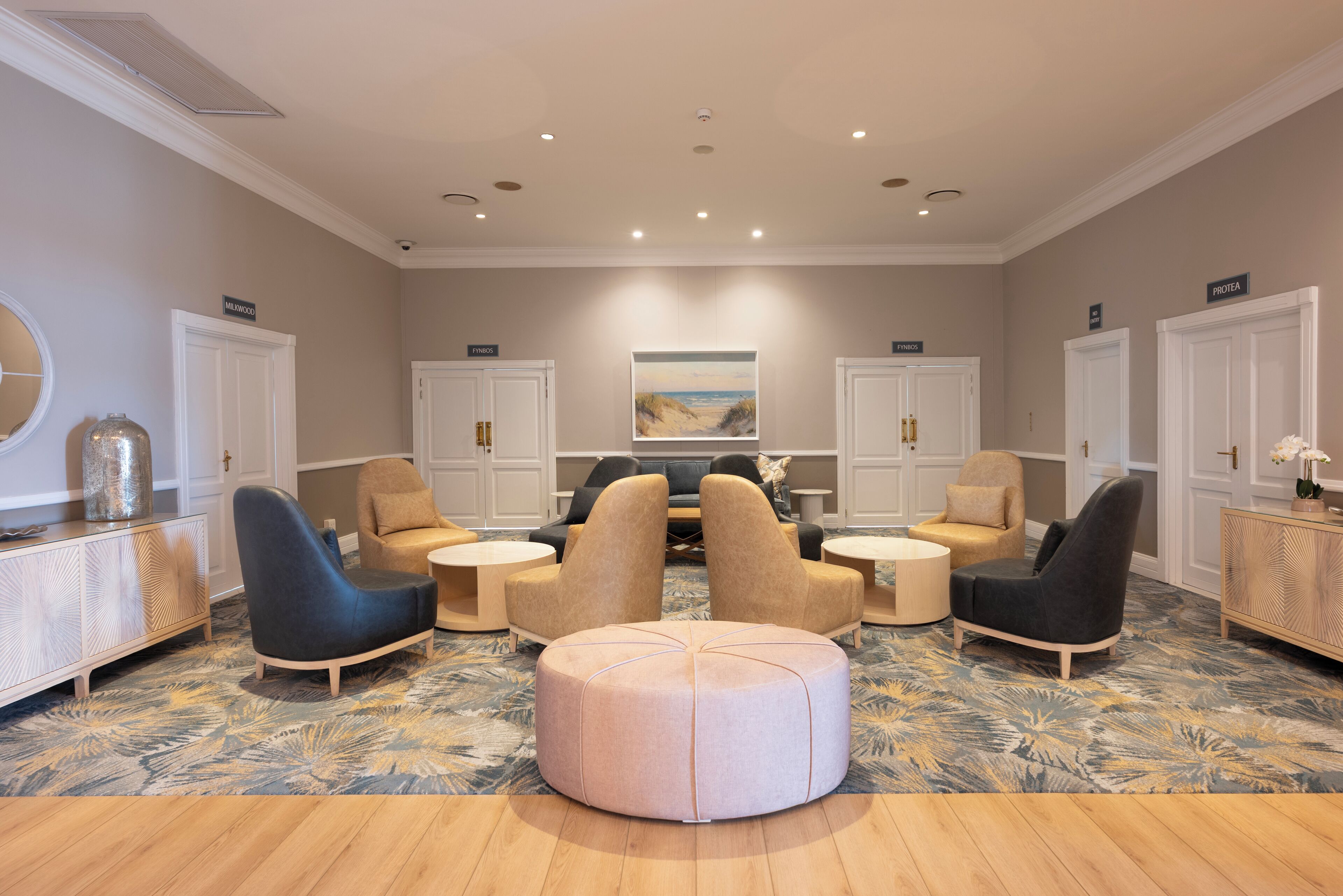 A spacious lounge area with a central seating arrangement, a large painting on the wall, and a decorative mirror on the left.