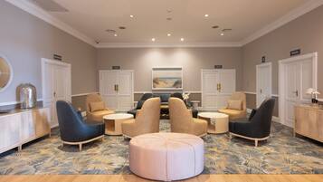 A spacious lounge area with a central seating arrangement, a large painting on the wall, and a decorative mirror on the left.