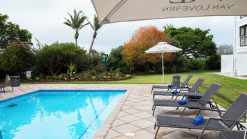 A swimming pool with lounge chairs and an umbrella.