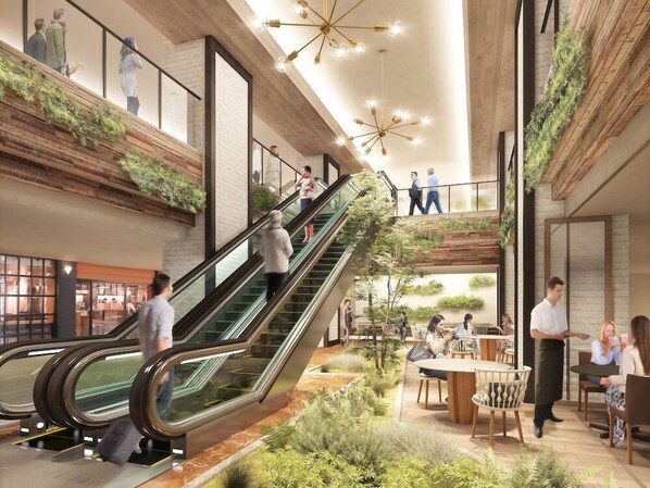 A modern indoor space with a central escalator, surrounded by seating areas and greenery.