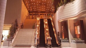 A modern hotel lobby with a central staircase, escalators, and a curved ceiling with recessed lighting. - Hotel Centraza Hakata (Fukuoka)