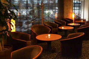 A cozy lounge area with comfortable seating and tables, large windows with blinds, and a city view. - Hotel Centraza Hakata (Fukuoka)