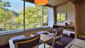 A room with a view of trees through large windows, a traditional Japanese-style table and chairs, and a hanging paper lantern.