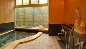 A wooden interior with a glass-enclosed hot tub, a window with a view of trees, and a shower area with a soap dispenser.