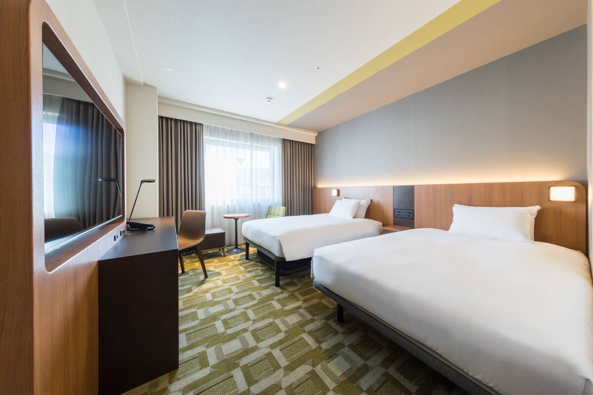 Ein Hotelzimmer mit zwei Betten, einem Schreibtisch, einem Stuhl, einem kleinen Tisch und einem großen Spiegel.