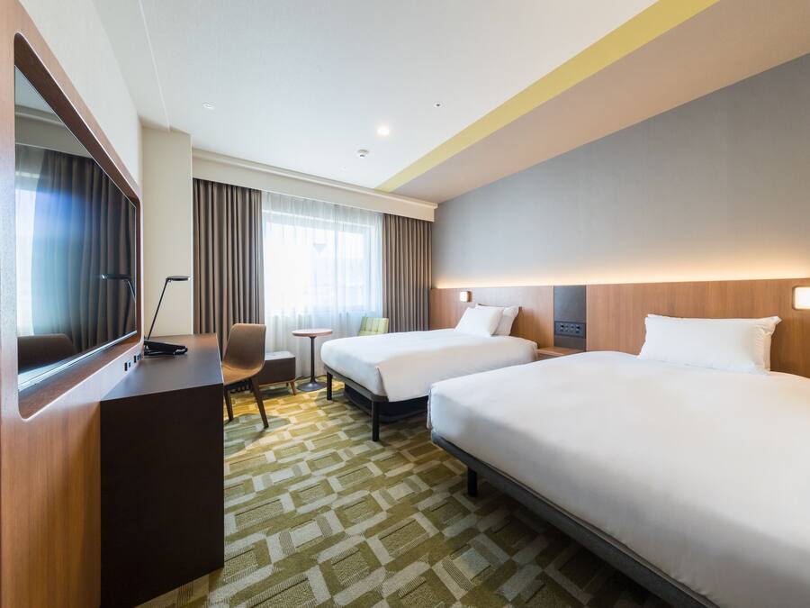 A hotel room with two beds, a desk, a chair, a small table, and a large mirror.