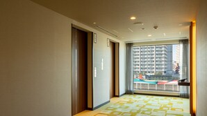 A hotel corridor with patterned carpet, a view of a cityscape through a large window, and a door leading to a room. - JR East Hotel Mets Akabane (Tokyo)