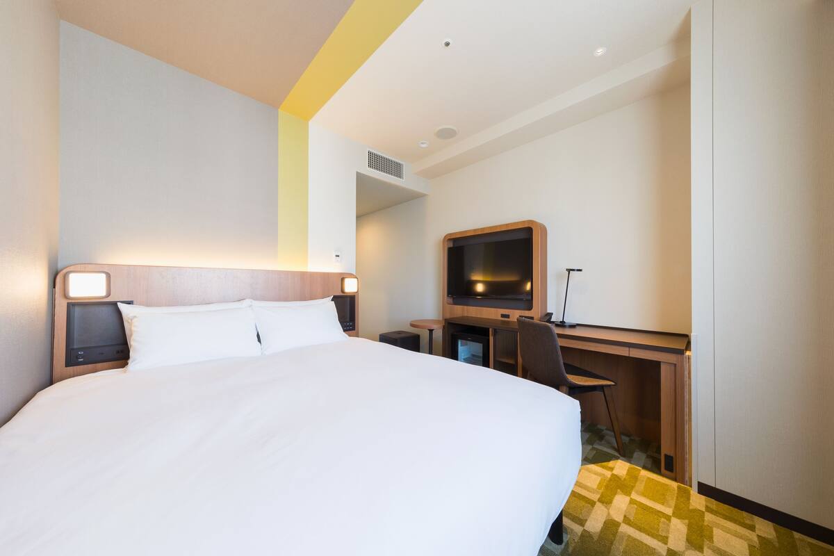 Ein Hotelzimmer mit einem großen Bett, einem Schreibtisch mit Stuhl, einem Fernseher und einem kleinen Tisch.