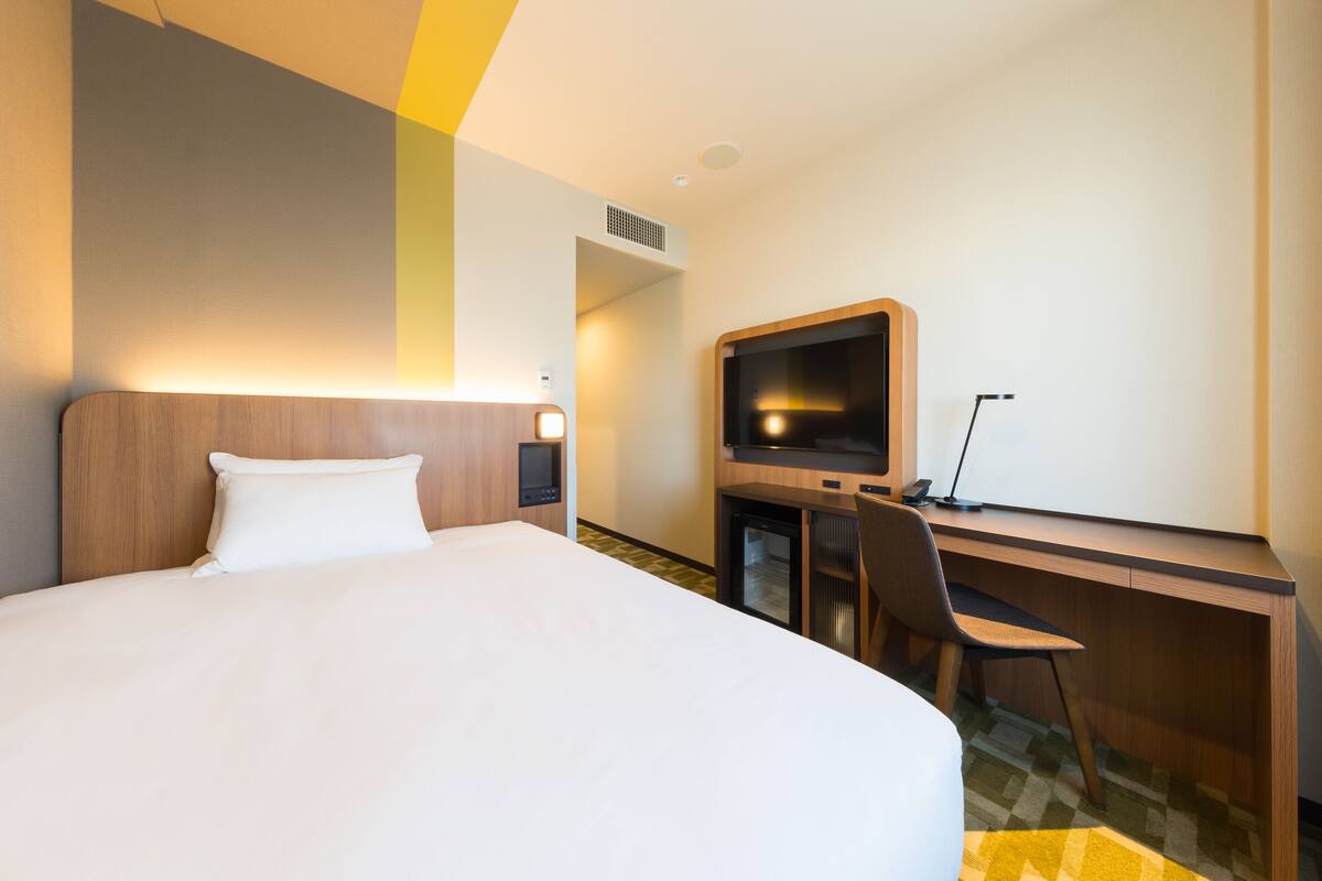 Ein Hotelzimmer mit einem großen Bett, einem Schreibtisch mit Computer und einem Fernseher.