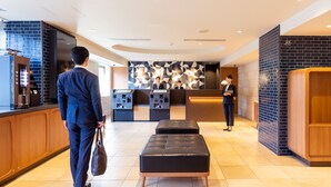 A modern hotel lobby with a reception desk, a seating area, and a coffee machine. - JR East Hotel Mets Akabane (Tokyo)