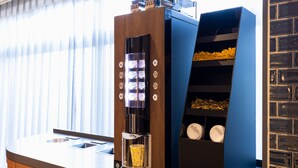 A coffee machine with a digital display and a cup holder, next to a blue storage unit with shelves. - JR East Hotel Mets Akabane (Tokyo)