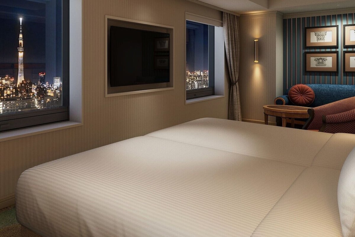 Ein Hotelzimmer mit einem großen Bett, einem Fernseher, Blick auf die Stadt, einem kleinen Tisch und einer Lampe.