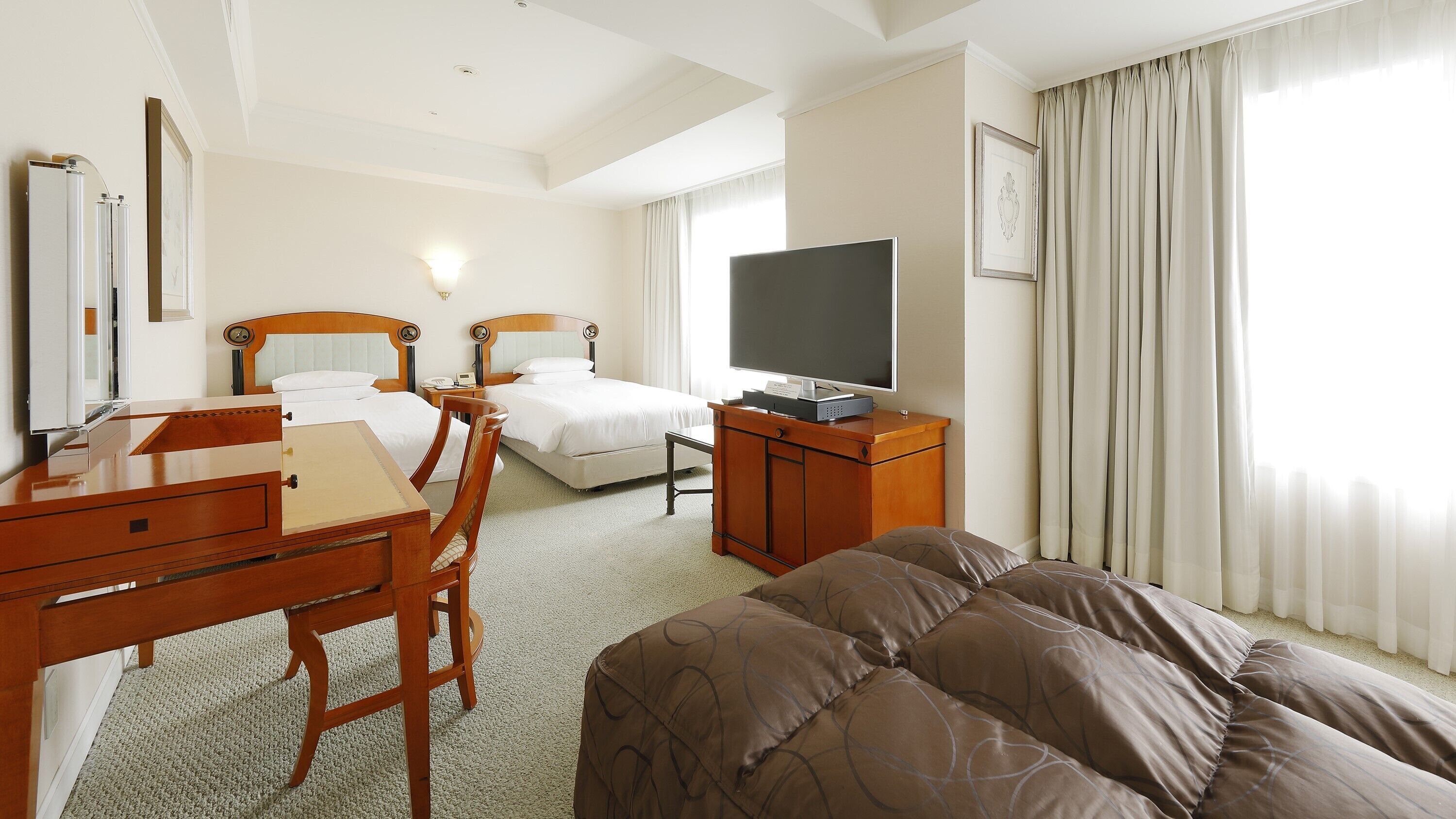 A hotel room with a bed, a desk, a chair, a television, and a window with curtains.