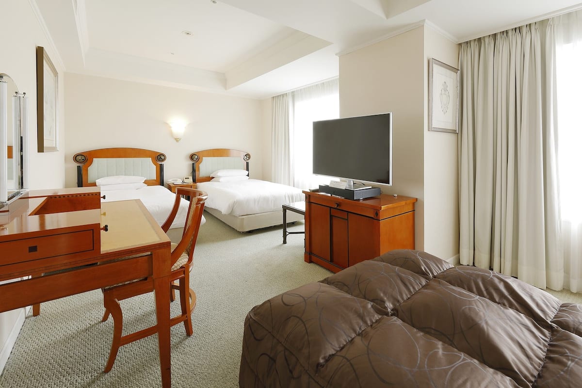 Ein Hotelzimmer mit Bett, Schreibtisch, Stuhl, Fernseher und einem Fenster mit Vorhängen.