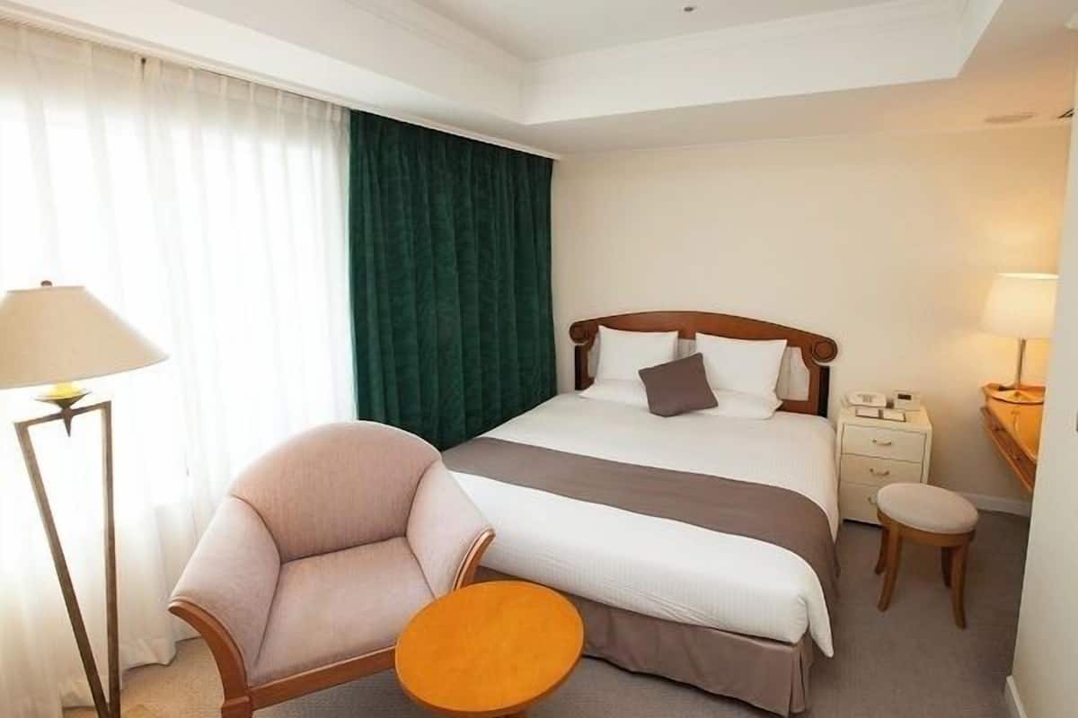 Ein Hotelzimmer mit Bett, Sessel, kleinem Tisch, Nachttisch und Lampe.