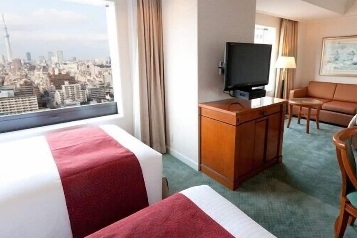 Ein Hotelzimmer mit Bett, Schreibtisch mit Fernseher, Sofa und Blick auf die Stadt.