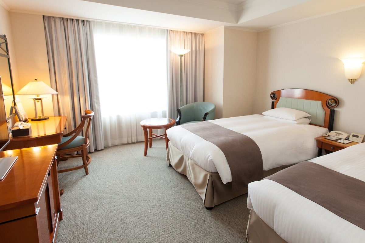 Ein Hotelzimmer mit zwei Betten, einem Schreibtisch, einem Stuhl, einer Lampe und einem Nachttisch mit Telefon.