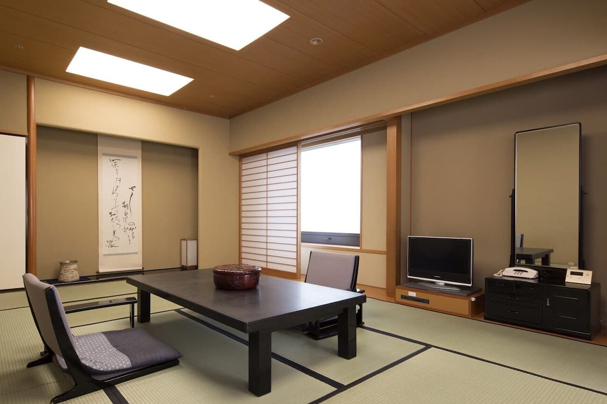 Ein traditioneller japanischer Raum mit Tatami-Böden, einem niedrigen Tisch, einem Stuhl, einem Fernseher und einem Schrank.